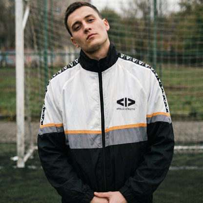 Man wearing a black and white jacket with orange accents on a sports field.