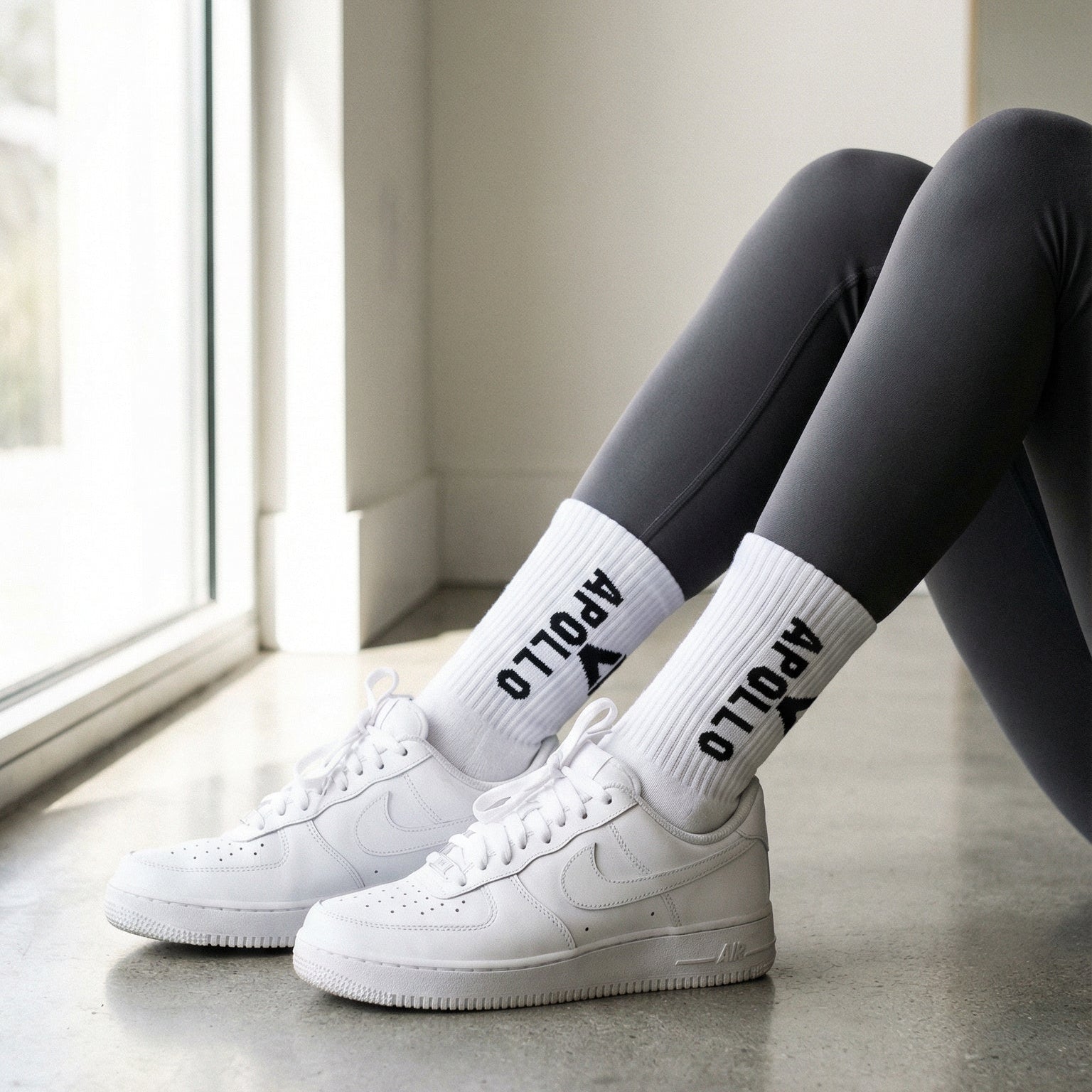 White sneakers and socks with text worn by a person sitting by a window.